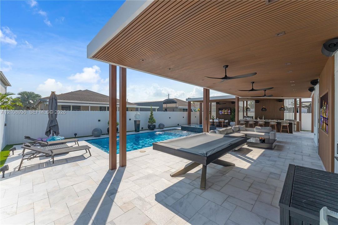 Covered outdoor living space featuring a wood-slat ceiling, recessed lighting, ceiling fans, stone paver patio, and an in-ground pool