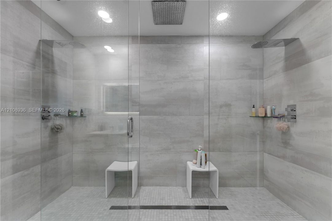 Walk-in shower featuring large-format wall tile, dual rainfall showerheads, a linear drain, and built-in glass shelving