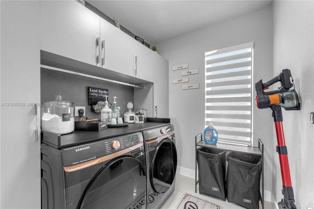 Laundry room featuring white wall-mounted cabinetry, matte black countertop, and a window with motorized zebra blinds