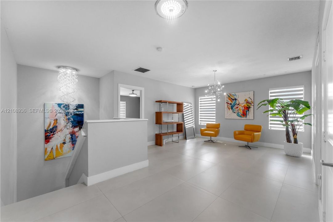 Open floor plan featuring large-format porcelain tile flooring, dual multi-tier crystal chandeliers, and dual-shade window treatments