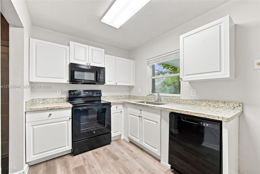 Kitchen featuring white shaker-style cabinetry, stone-finish countertops, black appliance package, undermount stainless steel sink, and wood-finish flooring
