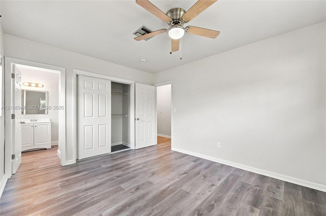 Neutral interior featuring wood-finish flooring, a ceiling fan with integrated lighting, and a reach-in closet with double doors