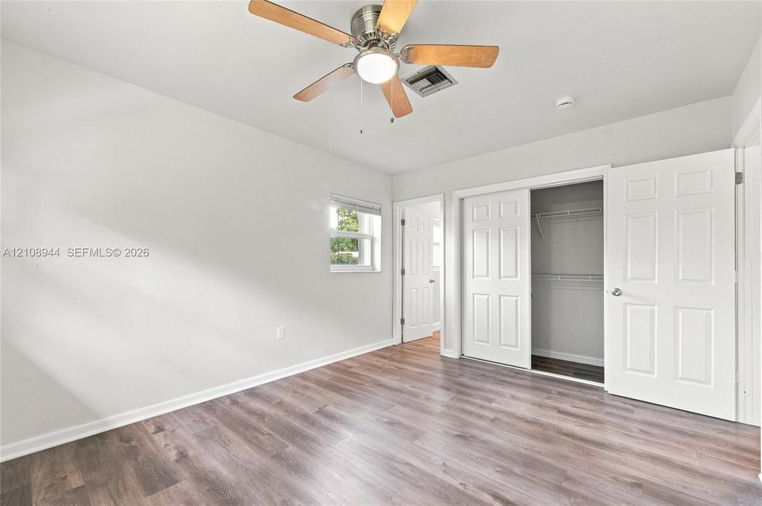 Neutral-toned room featuring wood-finish flooring, a ceiling fan with integrated lighting, and a closet with six-panel doors