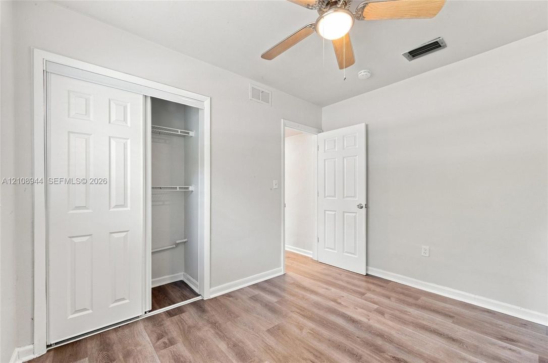 Room featuring wood-finish flooring, a ceiling fan with integrated lighting, and a closet with sliding doors and interior shelving