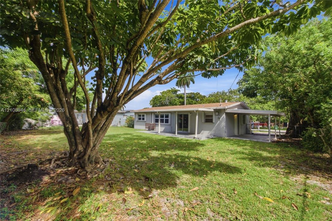 Exterior featuring a covered carport, concrete patio, mature landscaping, and an expansive lawn