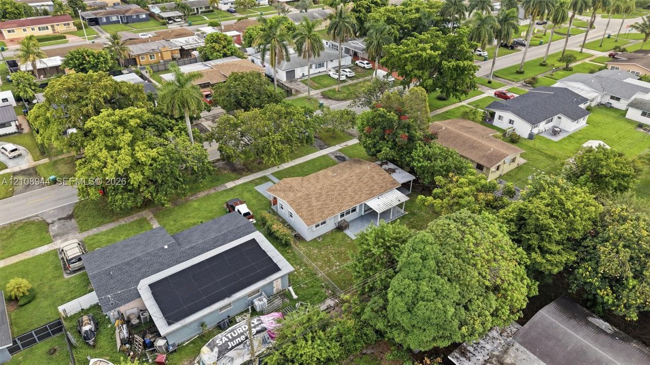 Aerial perspective of a residential property featuring a shingle roof, roof-mounted solar panels, an attached covered patio, and mature landscaping