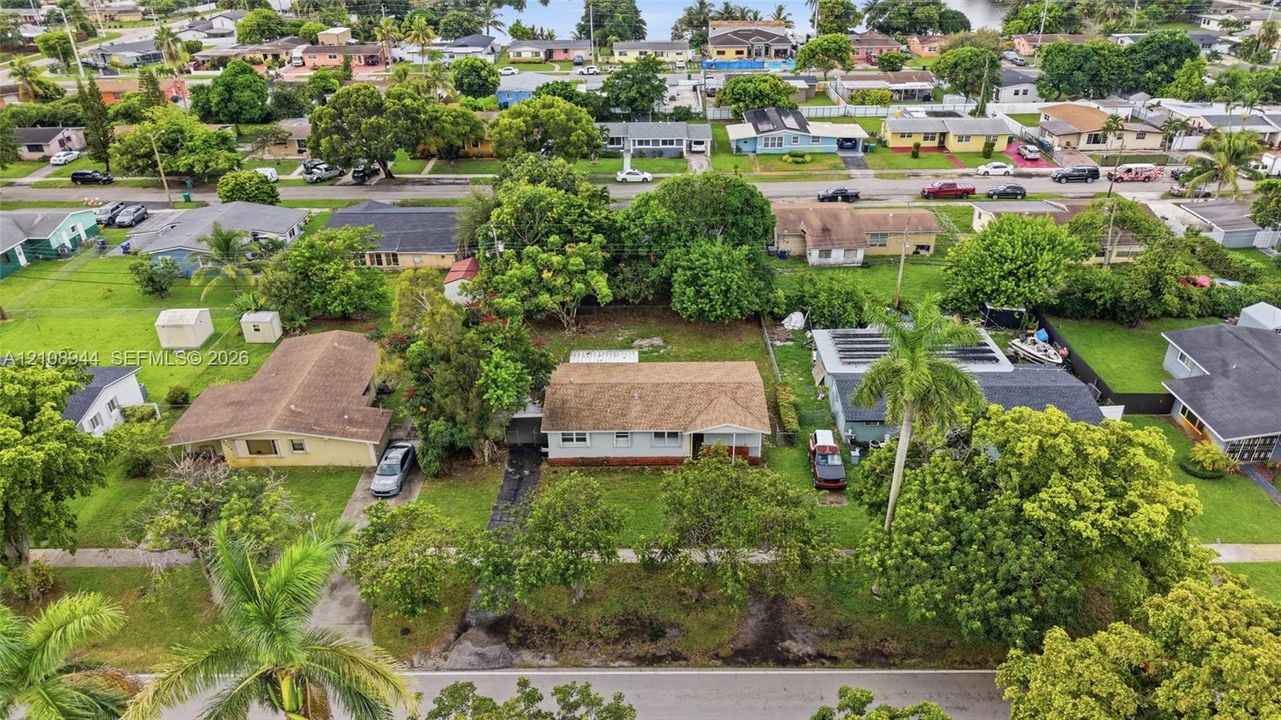 Aerial perspective of a single-story residence featuring a shingled roof, light-toned exterior siding, mature trees, and a grass-covered lot