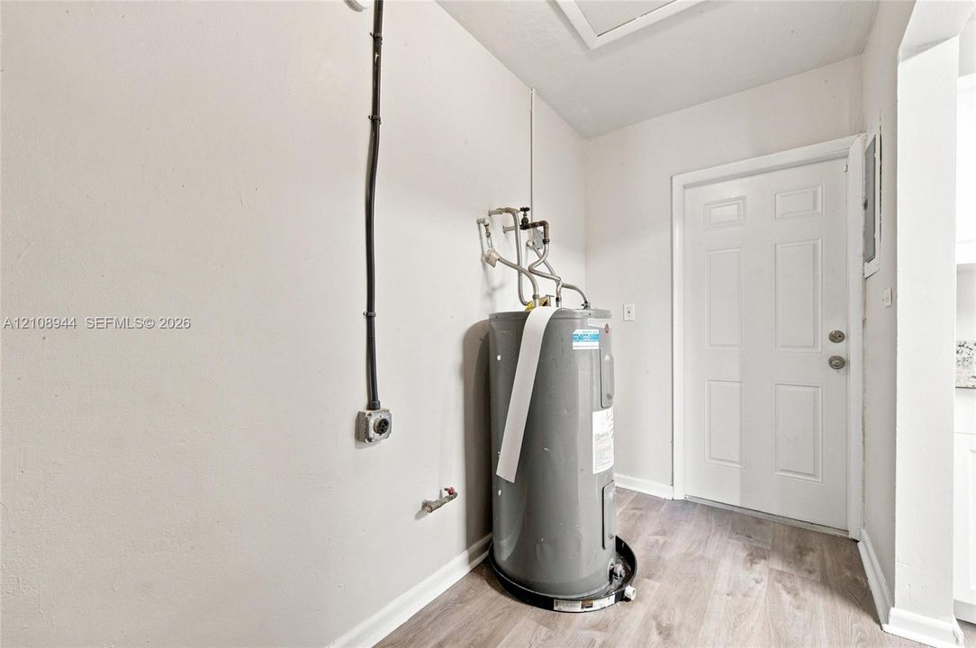 Utility area featuring wood-finish flooring, a six-panel door, and a dedicated water heater installation
