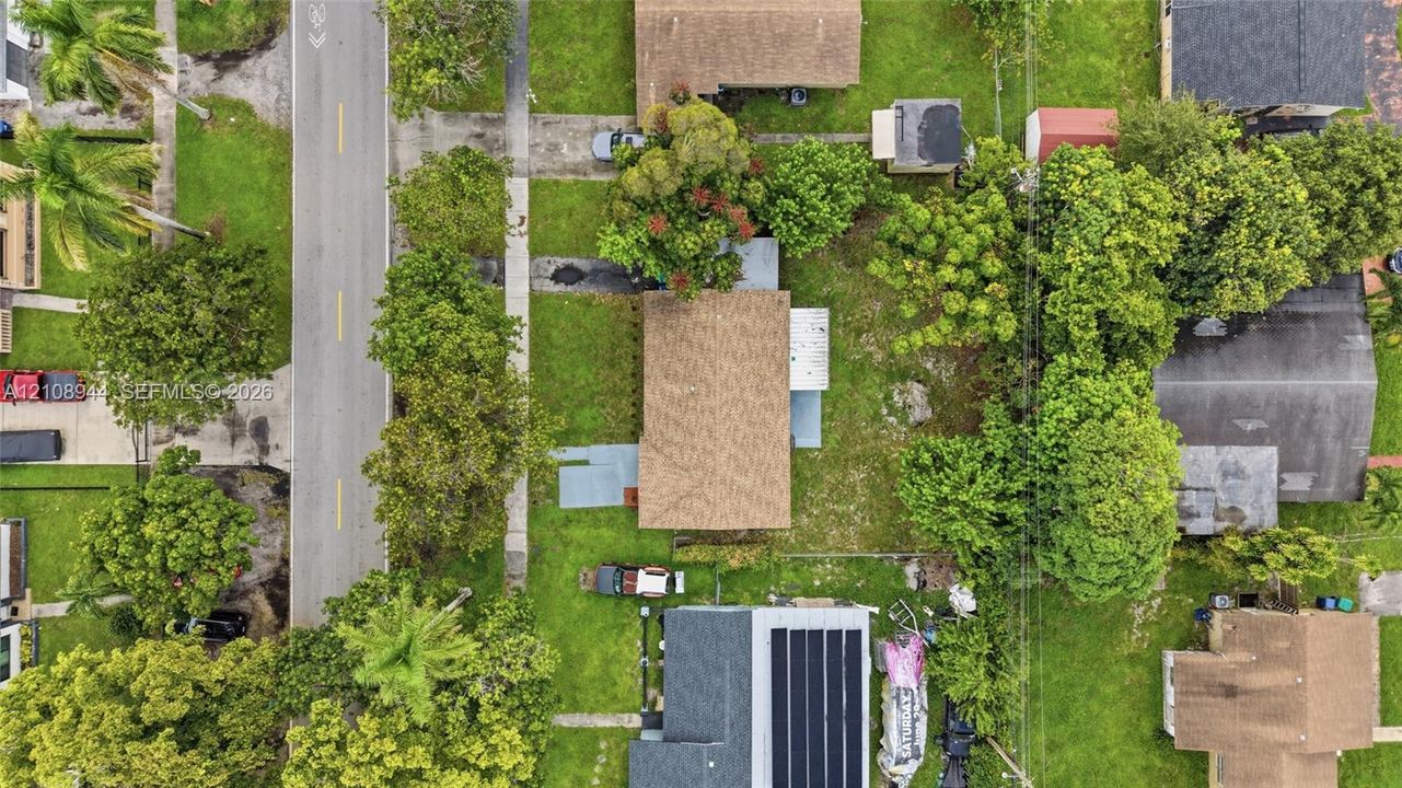 Aerial perspective of the property featuring a rectangular lot, mature trees, asphalt shingle roofing, and grass landscaping