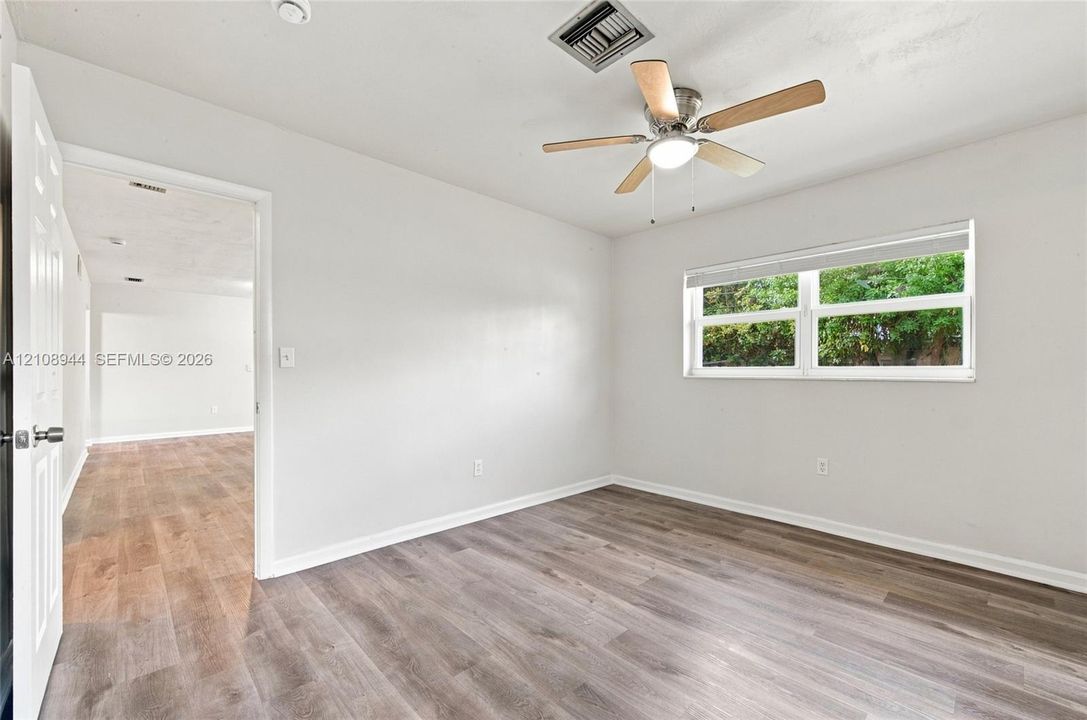 Wood-finish flooring, ceiling fan with integrated lighting, and natural light from a dual-pane window