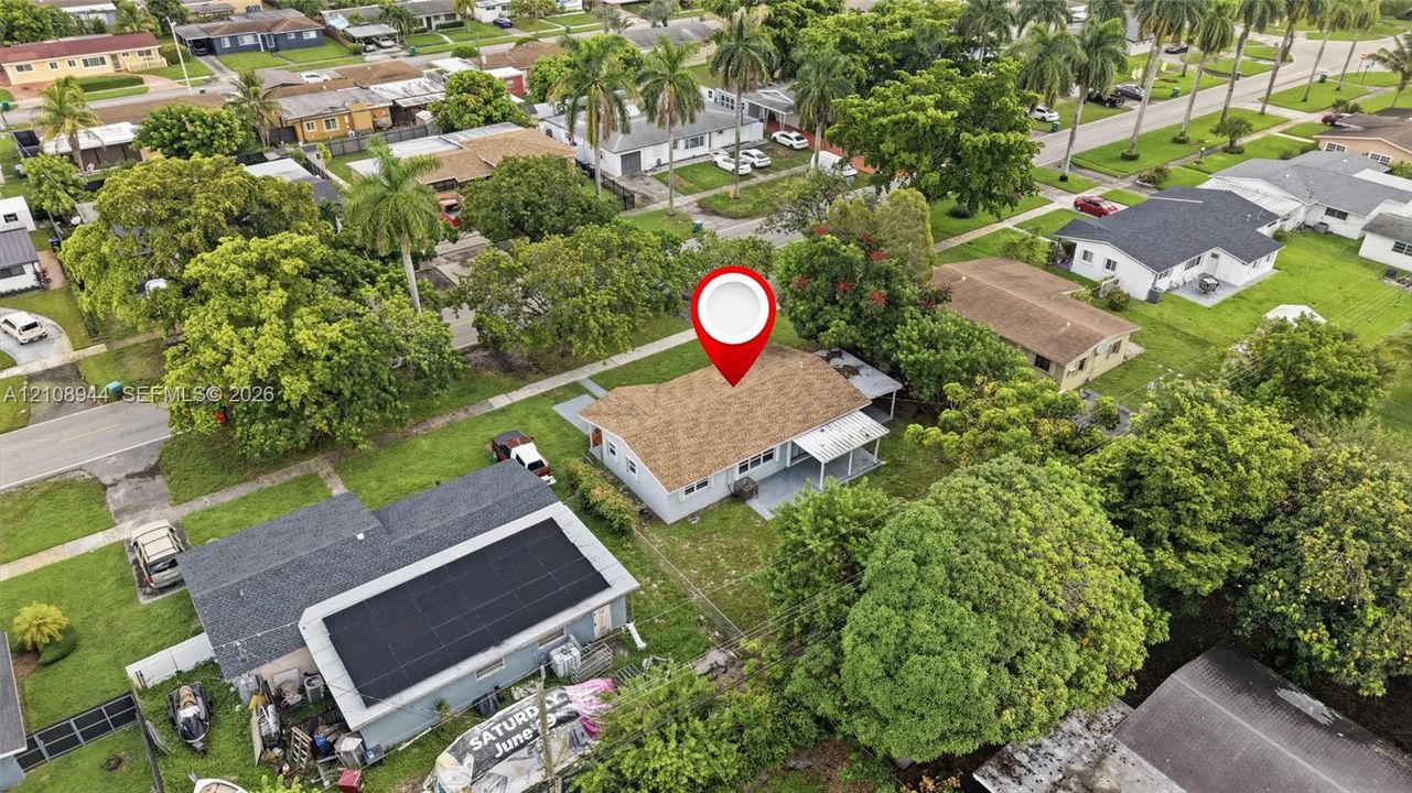 Aerial perspective of a detached single-story residence featuring a shingled roof, a covered concrete patio, and established mature landscaping