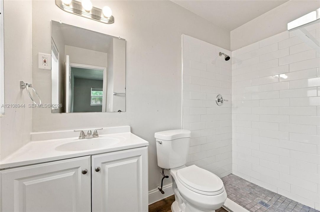 Bathroom featuring white subway tile shower surround, mosaic tile flooring, vanity with integrated basin, polished chrome hardware, and wall-mounted vanity mirror with integrated lighting