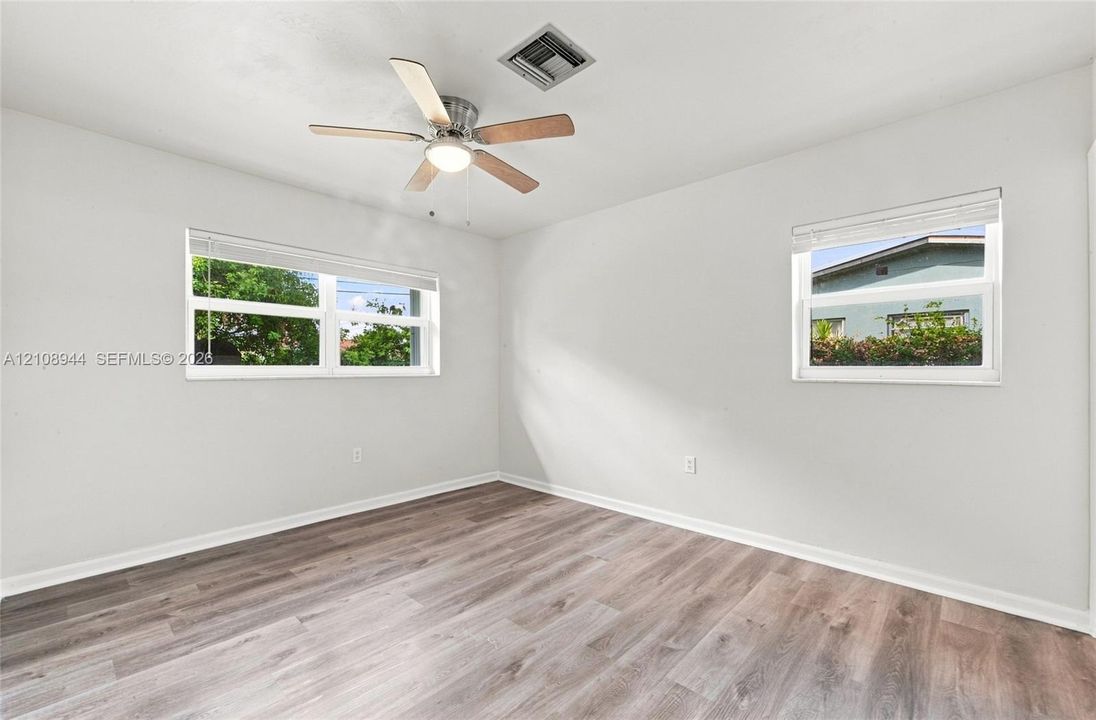 Room featuring wood-finish flooring, dual windows with blinds, and a ceiling fan with integrated lighting