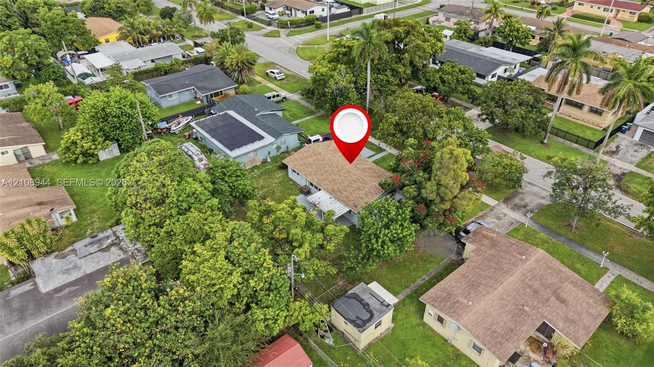 Aerial perspective of residential property featuring a pitched roof, attached carport, concrete driveway, and mature landscaping