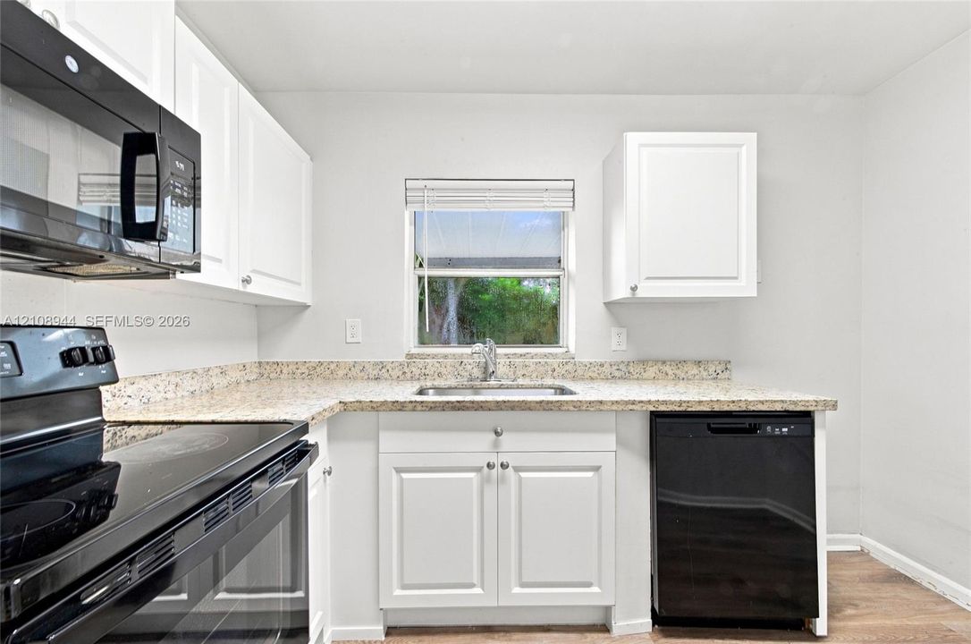 Kitchen featuring white cabinetry, stone-finish countertops, black built-in appliances, a stainless steel sink with a pull-down faucet, and wood-finish flooring