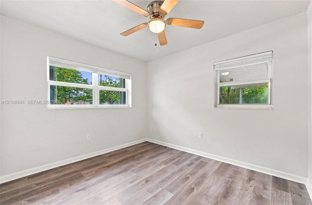 Interior room featuring wood-finish flooring, two dual-pane windows, and a ceiling fan with integrated lighting