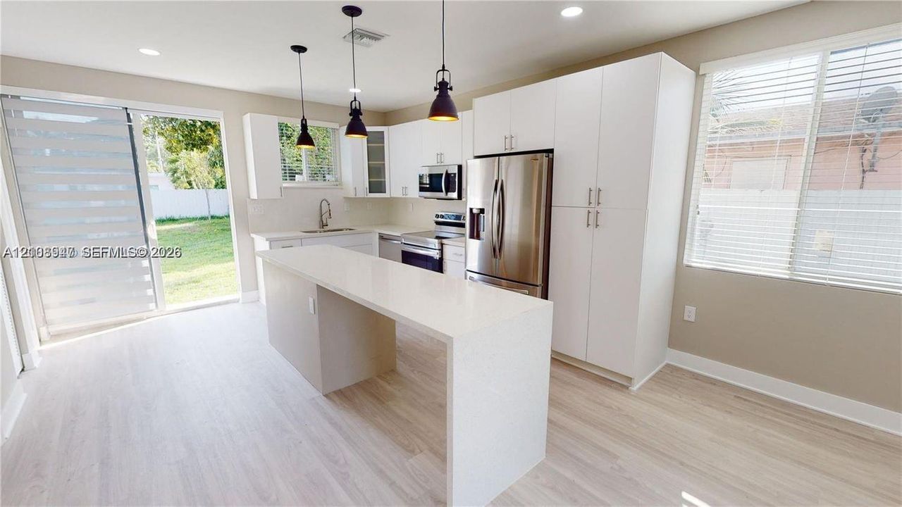 Kitchen featuring white cabinetry, an island with stone-finish countertops, stainless steel appliances, pendant lighting, and sliding glass doors