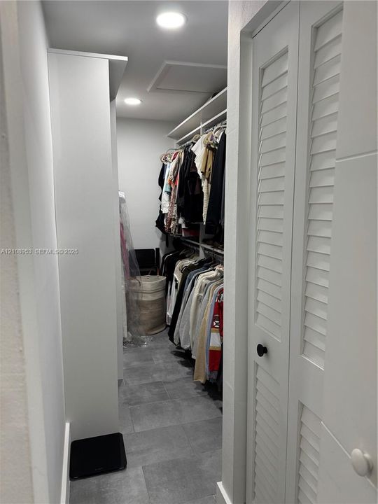 Walk-in storage space featuring ceramic tile flooring, built-in shelving, recessed lighting, and white louvered doors