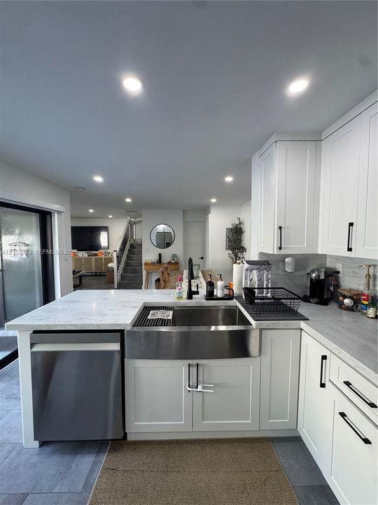 Kitchen featuring white shaker-style cabinetry, quartz countertops, a stainless steel apron-front sink with matte black hardware, integrated dishwasher, and recessed ceiling lighting