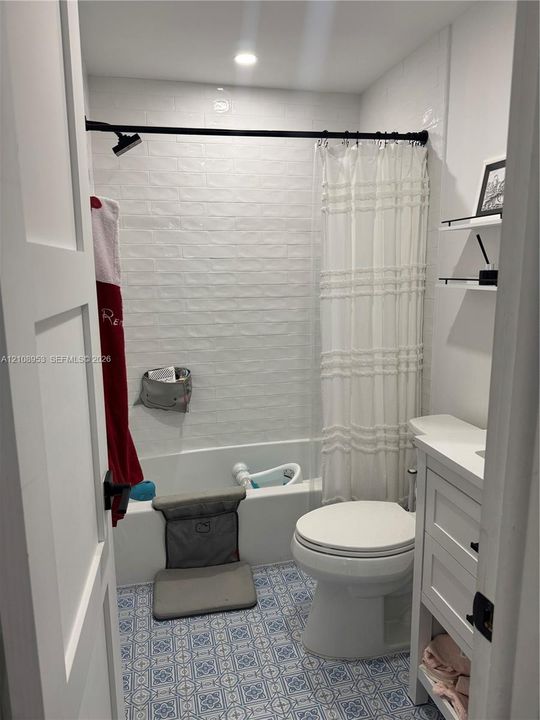 Bathroom featuring patterned floor tile, white subway tile shower surround, recessed ceiling lighting, a white vanity with integrated cabinetry, and matte black hardware