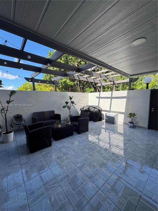 Covered patio featuring stone-patterned tile flooring, a custom wooden pergola, recessed lighting, and high perimeter privacy walls