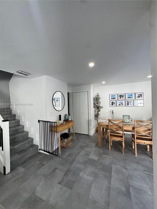 Large-format neutral-tone tile flooring, recessed ceiling lighting, and staircase with dark stone-finish treads and white wooden railings