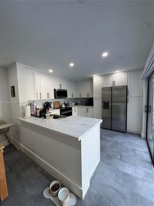 Kitchen featuring white shaker-style cabinetry, stone-finish countertops, stainless steel side-by-side refrigerator, recessed ceiling lighting, and large-format tile flooring