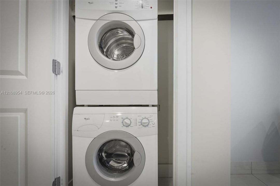 Stacked white front-loading washer and dryer unit housed within a dedicated closet