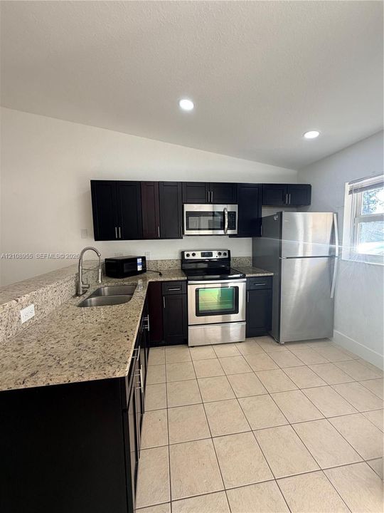 Kitchen featuring dark cabinetry, stone-surface countertops, tile flooring, recessed lighting, and stainless steel appliances