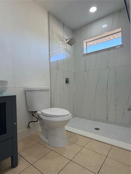 Walk-in shower featuring large-format wall tile with a veined pattern, hexagonal mosaic floor tile, rainfall showerhead, and horizontal transom window