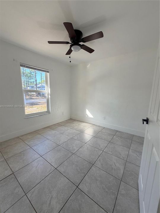Neutral-toned tile flooring, single-hung window with horizontal blinds, ceiling fan with integrated lighting, and matte black door hardware