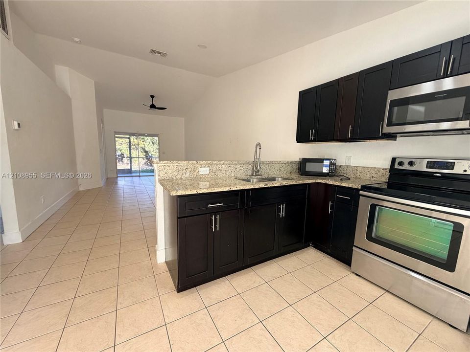 Kitchen featuring dark cabinetry, stone-finish countertops, stainless steel appliances, ceramic tile flooring, and a vaulted ceiling