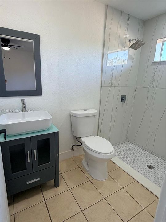 Bathroom featuring a dark-toned vanity with a rectangular vessel sink, tall chrome faucet, large-format tile shower surround, hexagonal floor tiling, and a dark-framed wall mirror