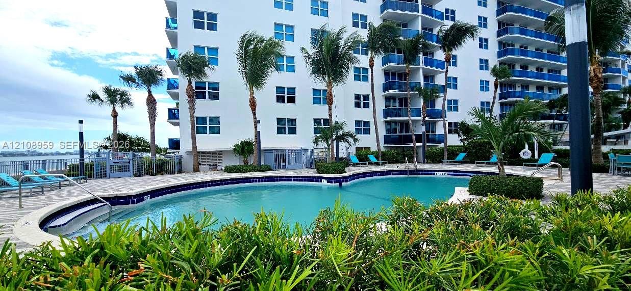 Resort-style pool featuring stone-paver decking, mature palm landscaping, and metal perimeter fencing
