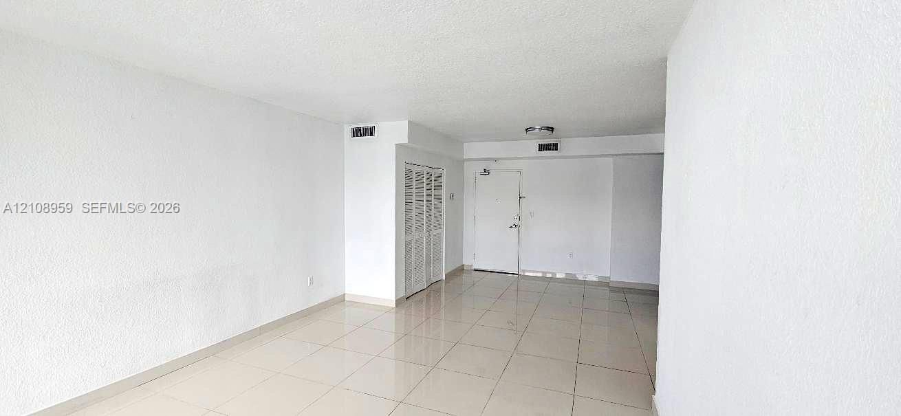 Open-concept interior featuring light-toned tile flooring, textured wall finishes, and white louvered closet doors