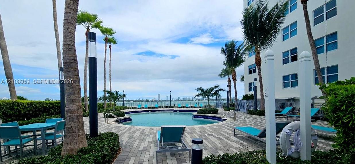 Swimming pool with surrounding paver deck, palm trees, and water backdrop