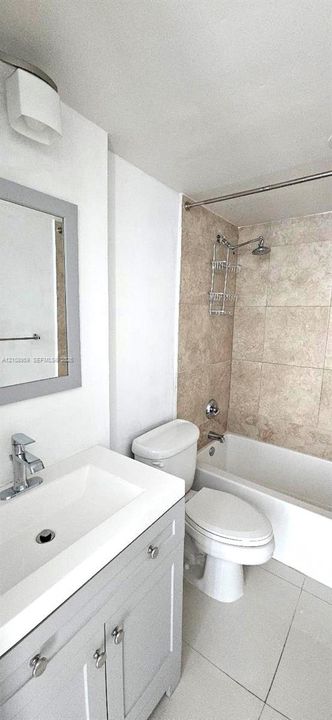 Bathroom featuring a grey vanity with an integrated rectangular sink, stone-finish wall tile in the shower enclosure, a chrome shower fixture, and tile flooring