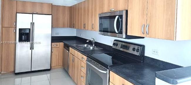 Kitchen featuring wood-finish cabinetry, stainless steel appliances, a double-basin sink with a gooseneck faucet, and dark countertops