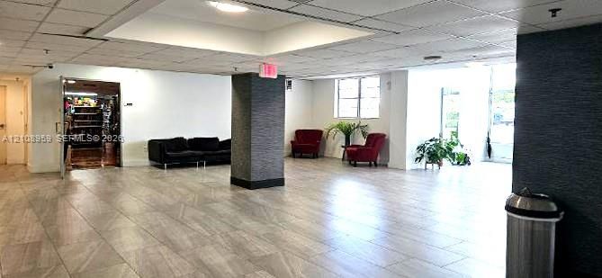 Open floor plan featuring large-format ceramic tile flooring, recessed tray ceiling, and textured wall coverings on structural pillars