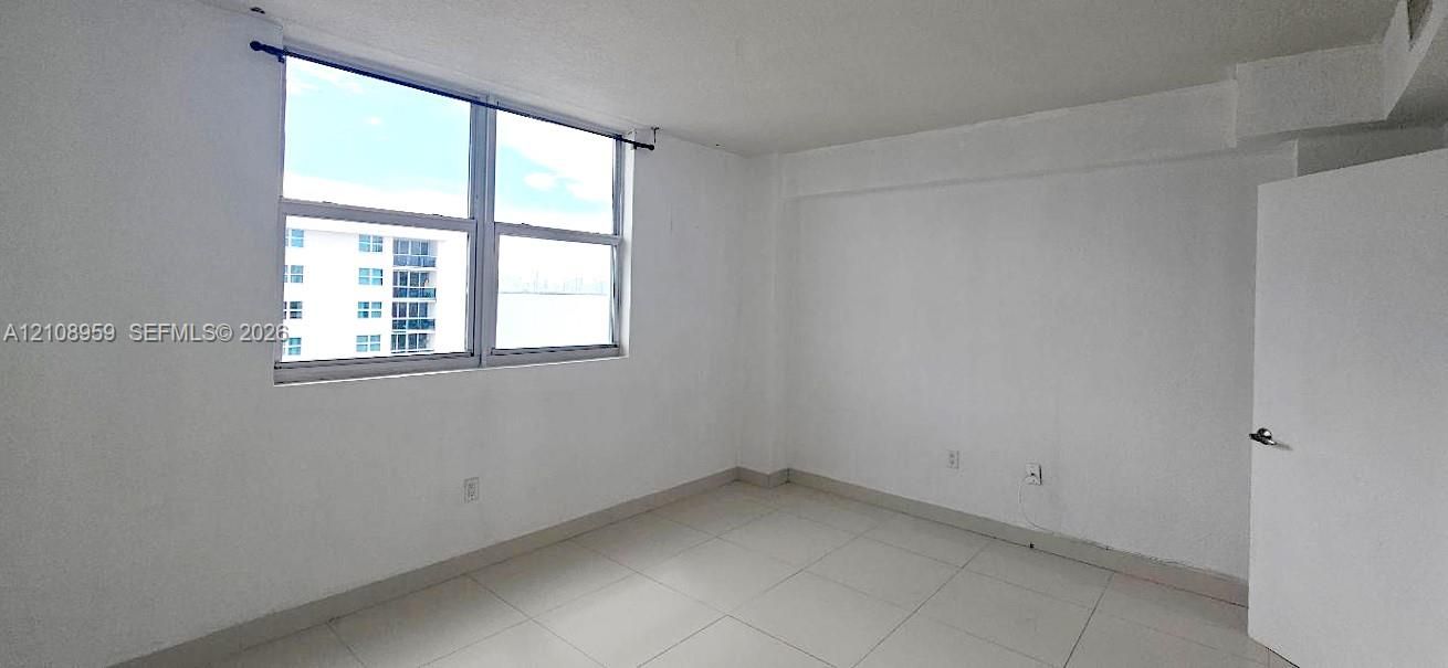Room featuring white walls, large window with a horizontal pane, and neutral-tone tile flooring