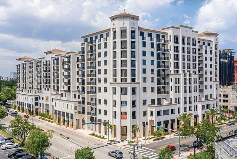 Mid-rise building featuring a light-colored stucco exterior, decorative corner turrets, tiered balconies with wrought-iron railings, and ground-level retail awnings
