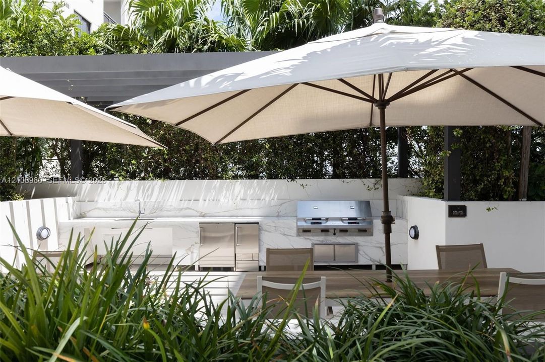 Outdoor kitchen featuring stone-surface countertops, built-in stainless steel grill, stainless steel under-counter refrigerator, sink, and overhead pergola structure