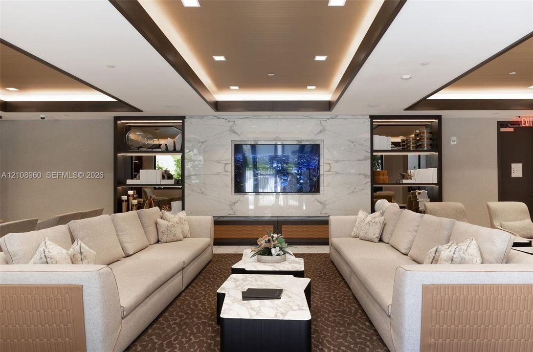 Tray ceiling with recessed lighting, integrated stone-finish media wall, and built-in display cabinetry with accent lighting