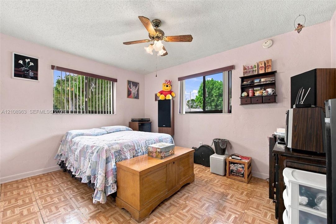 Interior room featuring parquet flooring, dual windows with horizontal blinds, and a ceiling-mounted fan with light fixture