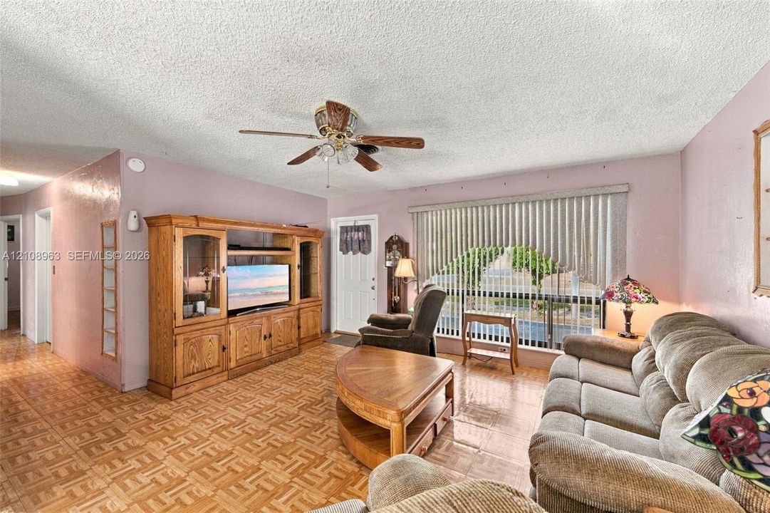 Living area featuring parquet flooring, built-in wooden cabinetry, a ceiling fan with integrated lighting, and vertical window blinds