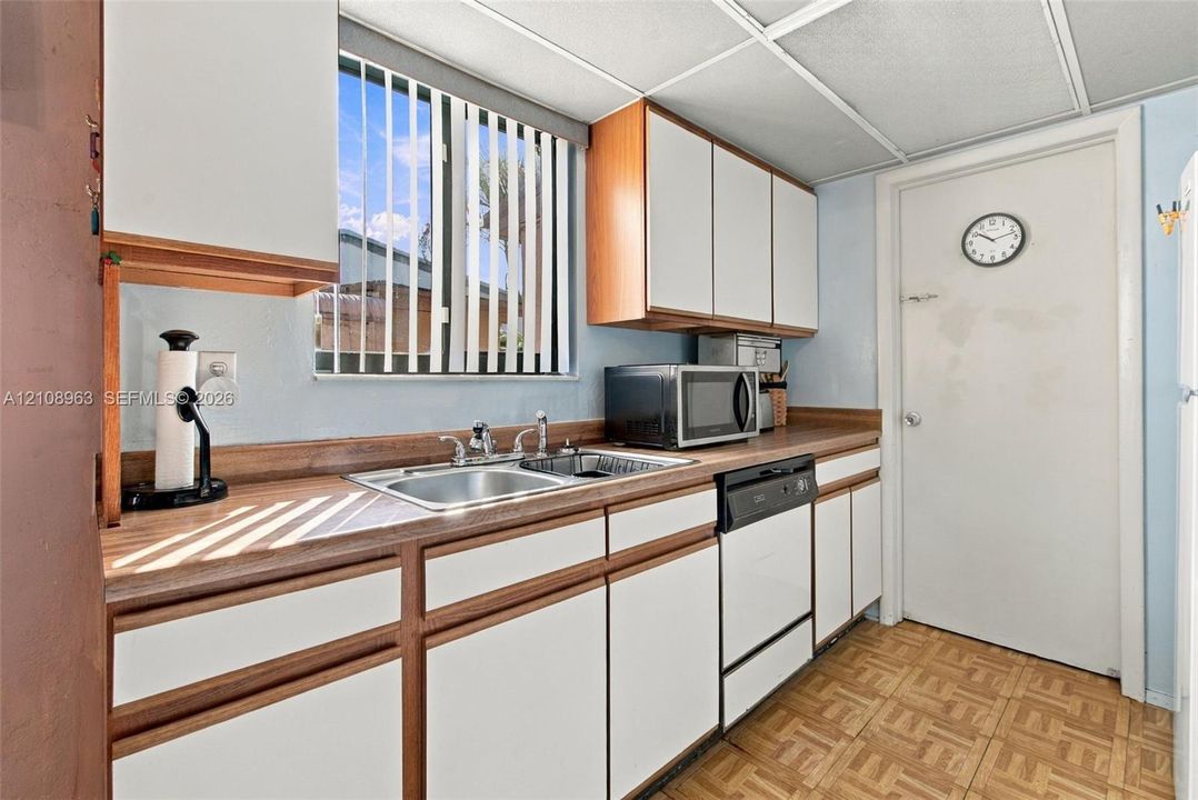 Kitchen featuring white cabinetry with wood trim, wood-finish countertops, stainless steel dual-basin sink, built-in dishwasher, and patterned tile flooring