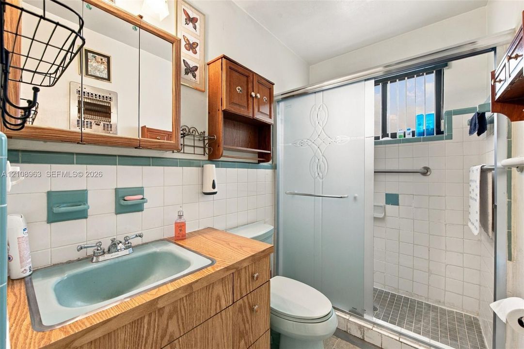 Bathroom featuring a wood vanity with a dual-handle faucet, integrated medicine cabinet, shower enclosure with glass sliding doors, and tiled wall accents