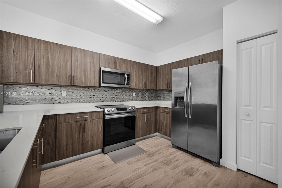 Kitchen featuring wood-finish cabinetry, white countertops, mosaic tile backsplash, stainless steel appliances, and wood-finish flooring