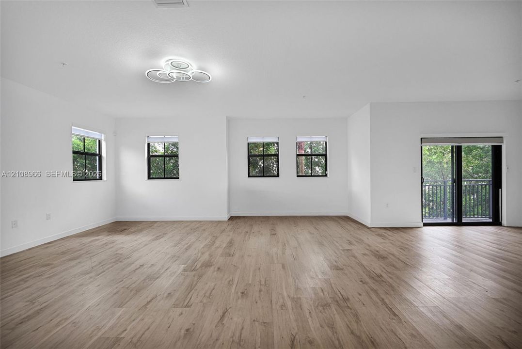Spacious interior featuring wood-finish flooring, recessed lighting, neutral white walls, multiple windows with black trim, and a glass sliding door
