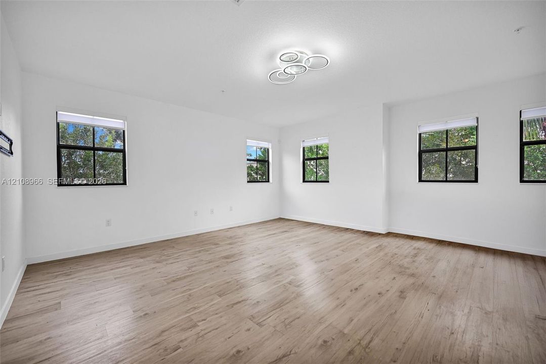 Wood-finish flooring, four windows with black frames, and modern multi-ring flush-mount lighting
